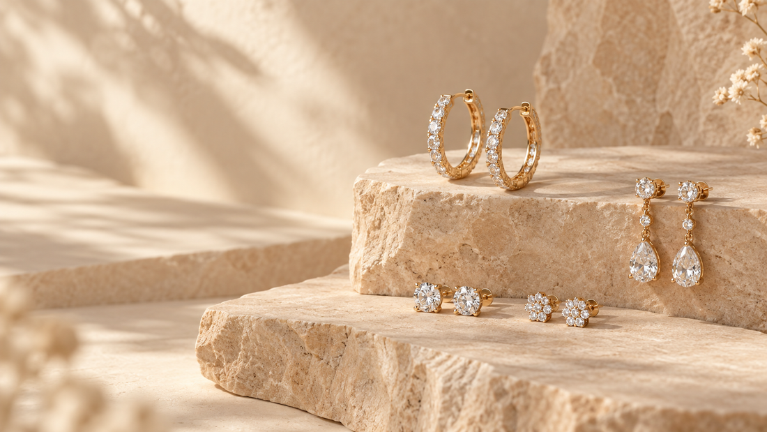 Gold-tone cubic zirconia hoop, drop and stud earrings arranged on warm sandstone